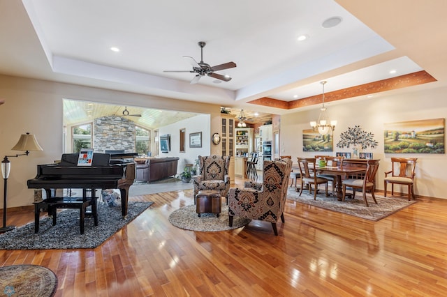 dining space with a tray ceiling, ceiling fan with notable chandelier, hardwood / wood-style flooring, and vaulted ceiling