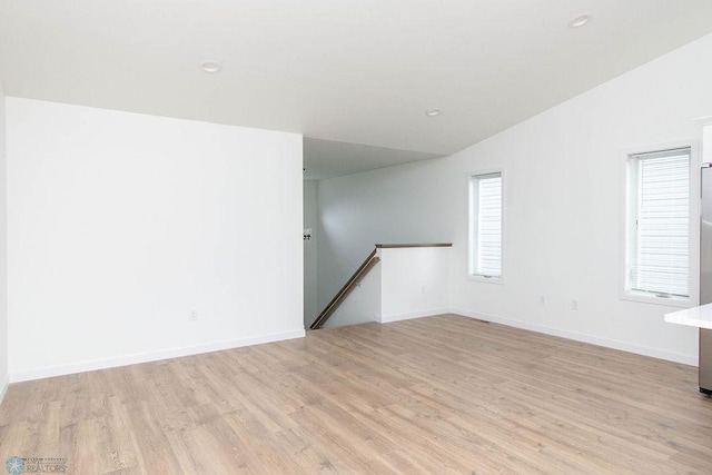 empty room with light wood-type flooring, vaulted ceiling, and a healthy amount of sunlight