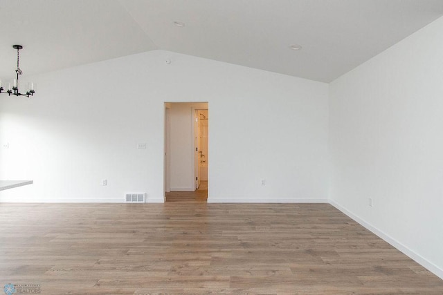 spare room featuring vaulted ceiling, an inviting chandelier, and light hardwood / wood-style flooring