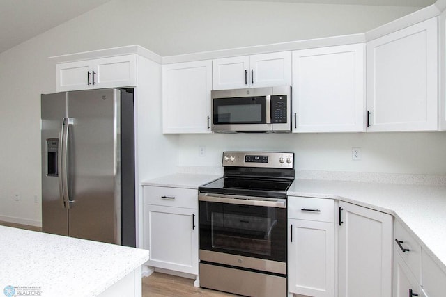 kitchen with appliances with stainless steel finishes, vaulted ceiling, white cabinets, and light hardwood / wood-style floors