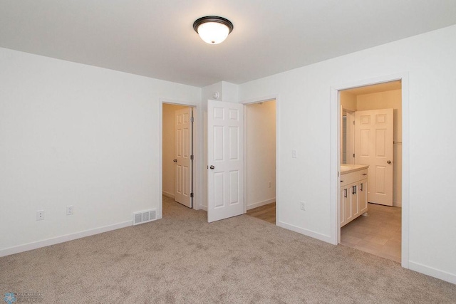 unfurnished bedroom featuring light colored carpet and ensuite bath