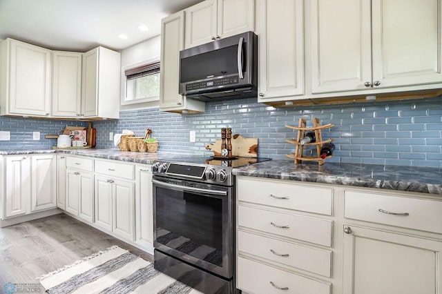 kitchen with dark stone counters, light hardwood / wood-style flooring, stainless steel appliances, backsplash, and white cabinets