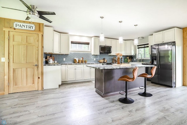 kitchen featuring light stone counters, hanging light fixtures, a kitchen island, light hardwood / wood-style flooring, and black fridge with ice dispenser