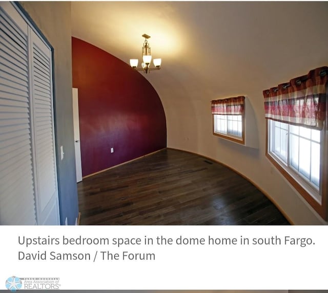 spare room with a notable chandelier and dark wood-type flooring