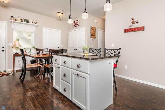 kitchen with dark stone countertops, a center island, decorative light fixtures, dark wood-type flooring, and a kitchen breakfast bar