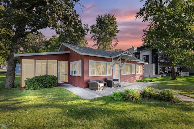 back house at dusk featuring a sunroom, a lawn, and cooling unit