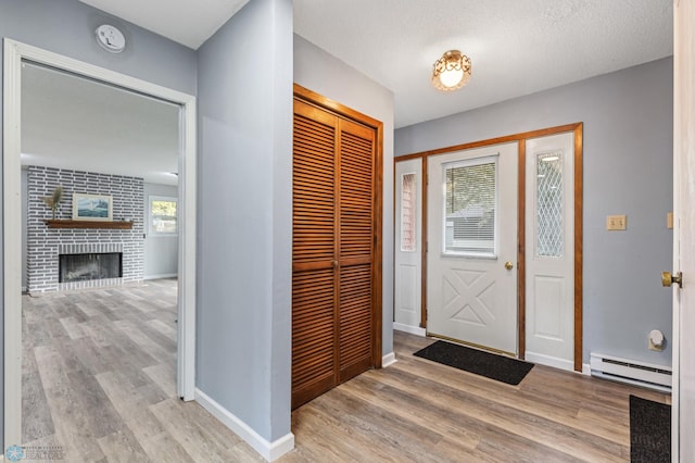 foyer entrance with a baseboard heating unit, a fireplace, a textured ceiling, and light hardwood / wood-style floors