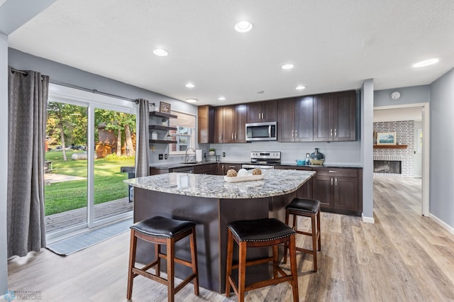 kitchen with light wood-type flooring, a fireplace, a kitchen island, a breakfast bar, and appliances with stainless steel finishes