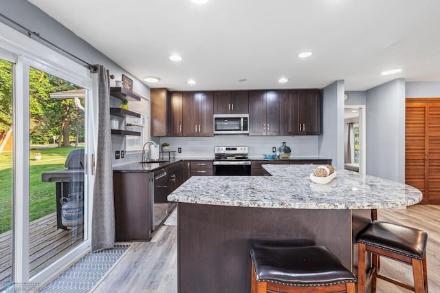 kitchen with light hardwood / wood-style flooring, stainless steel appliances, sink, light stone countertops, and a breakfast bar area