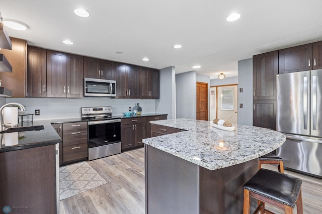 kitchen with a kitchen island, appliances with stainless steel finishes, light hardwood / wood-style floors, a kitchen bar, and sink