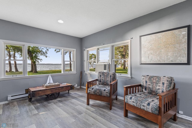 sitting room with a water view, a baseboard radiator, and hardwood / wood-style flooring