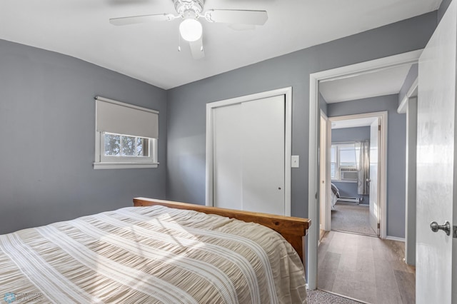 bedroom with a closet, wood-type flooring, a baseboard heating unit, and ceiling fan