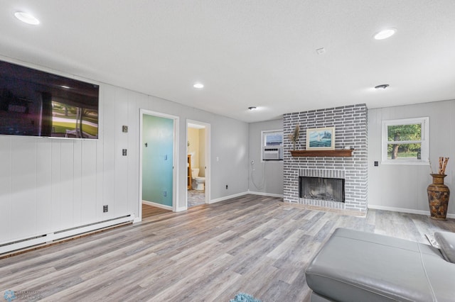 unfurnished living room featuring light hardwood / wood-style flooring, baseboard heating, and a brick fireplace