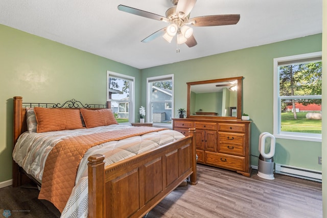 bedroom featuring multiple windows, baseboard heating, hardwood / wood-style flooring, and ceiling fan