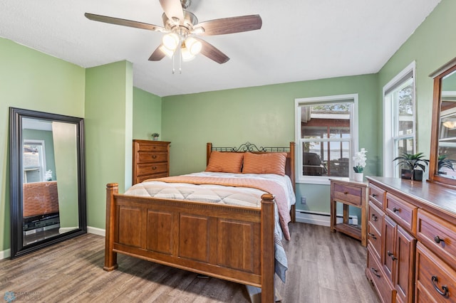 bedroom with multiple windows, ceiling fan, hardwood / wood-style flooring, and baseboard heating