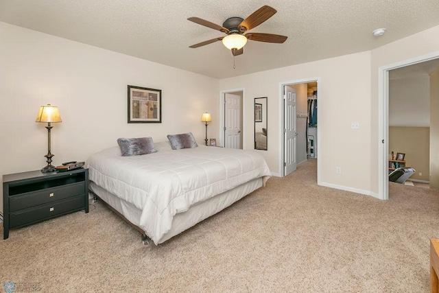 bedroom with light colored carpet, a spacious closet, ceiling fan, and a textured ceiling