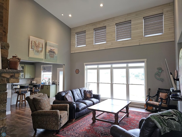 living room featuring a fireplace, a healthy amount of sunlight, a high ceiling, and dark wood-type flooring