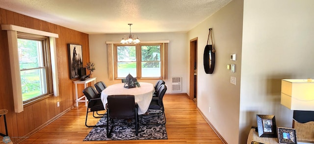 dining area featuring a wealth of natural light, light hardwood / wood-style flooring, wood walls, and a textured ceiling