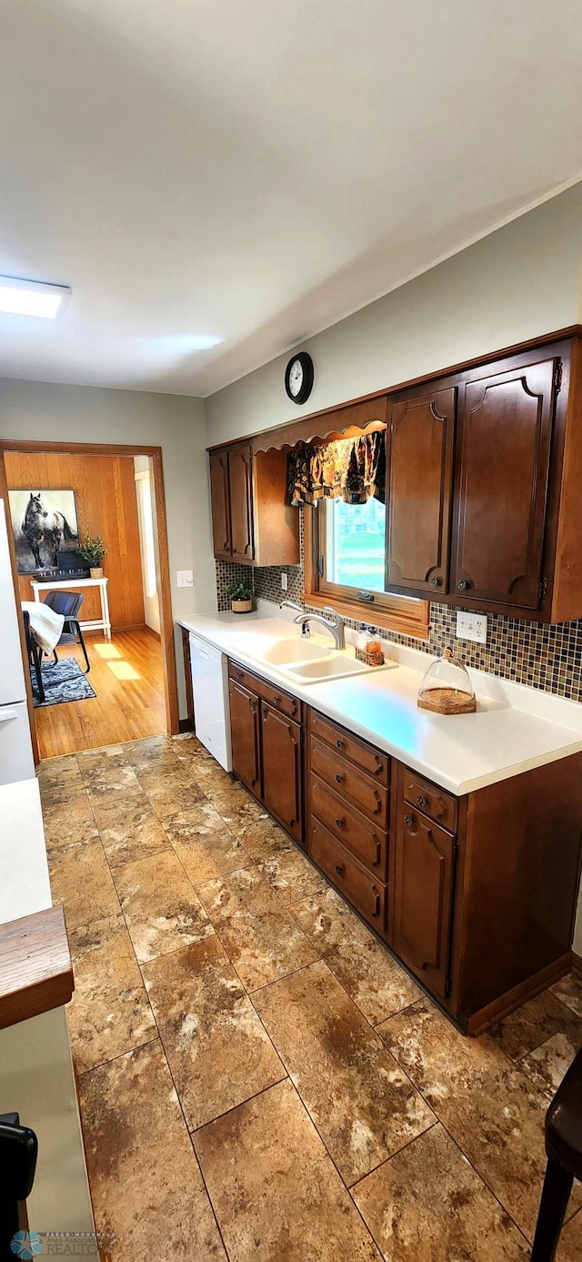 kitchen with dark brown cabinets, white dishwasher, hardwood / wood-style floors, tasteful backsplash, and sink