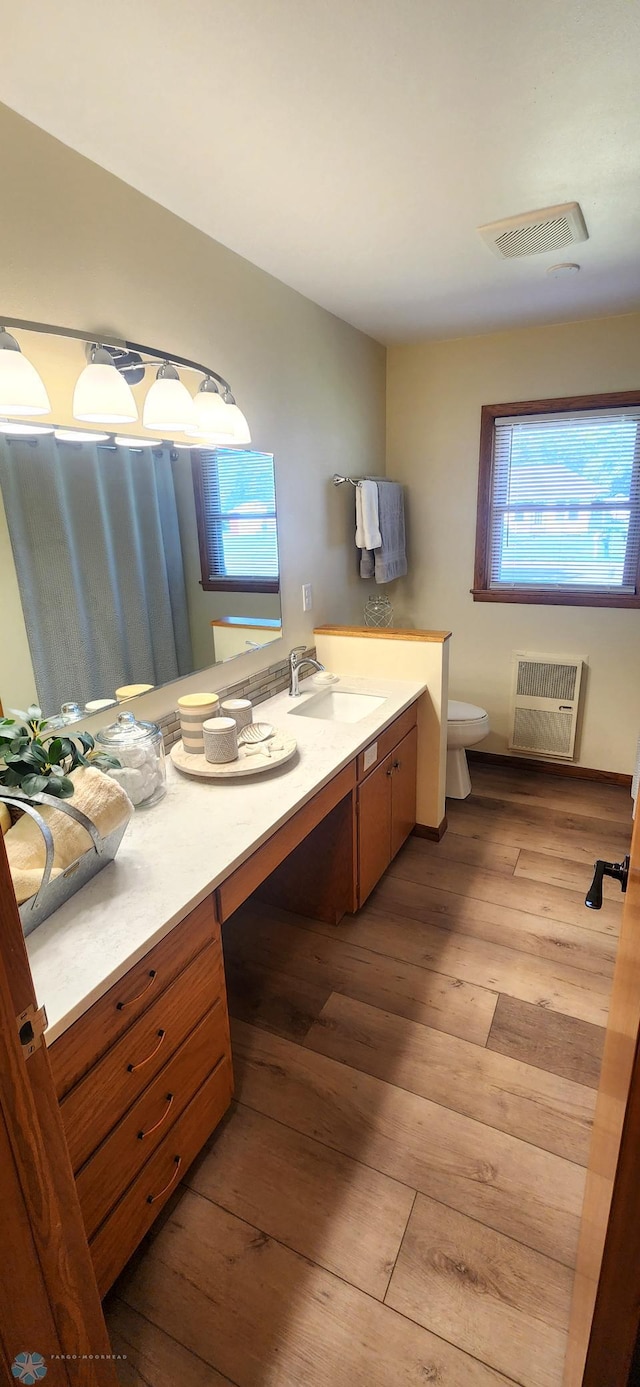 bathroom featuring toilet, vanity, heating unit, radiator, and hardwood / wood-style flooring