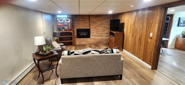 living room with a fireplace, wooden walls, light wood-type flooring, baseboard heating, and a paneled ceiling