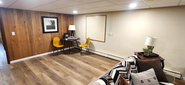 sitting room featuring wood-type flooring, baseboard heating, wood walls, and a paneled ceiling