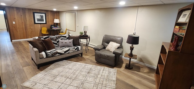 living room featuring light wood-type flooring, baseboard heating, wooden walls, and a drop ceiling