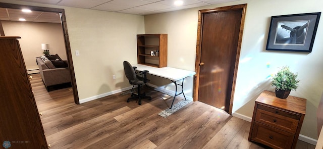 home office featuring a paneled ceiling, baseboard heating, and light wood-type flooring