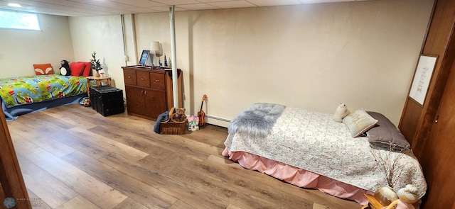 bedroom featuring light hardwood / wood-style flooring, a baseboard radiator, and a drop ceiling