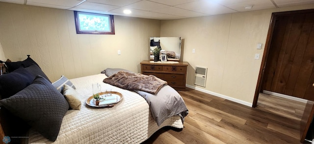 bedroom featuring dark hardwood / wood-style floors, heating unit, a drop ceiling, and wooden walls