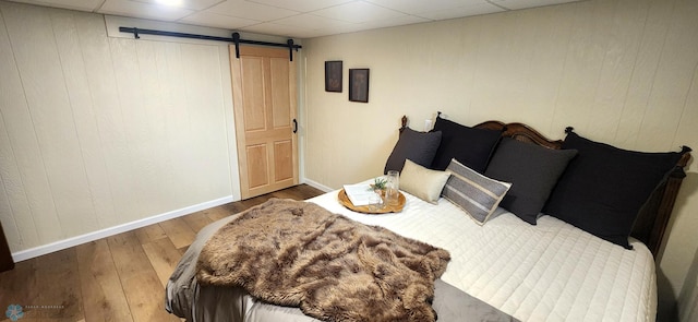 bedroom featuring a barn door, wood walls, wood-type flooring, and a drop ceiling