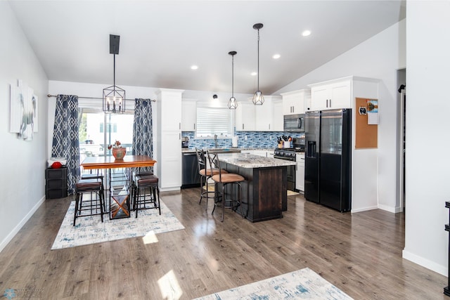 kitchen with hanging light fixtures, appliances with stainless steel finishes, a center island, a breakfast bar area, and vaulted ceiling