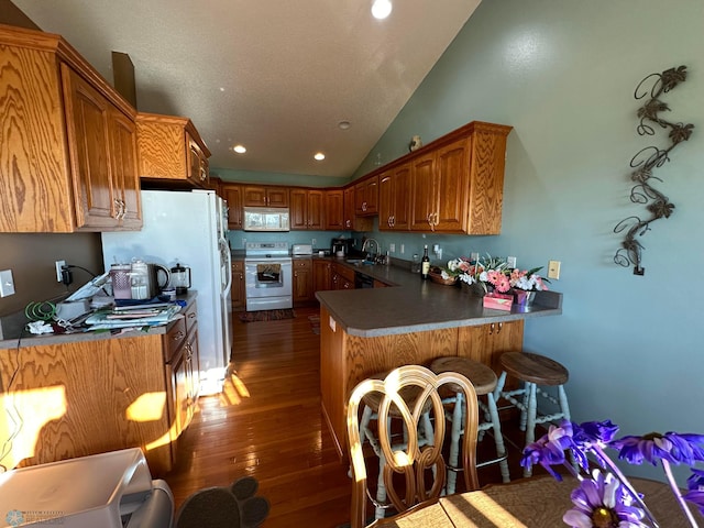 kitchen featuring vaulted ceiling, white appliances, dark wood-type flooring, kitchen peninsula, and sink