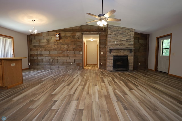 unfurnished living room featuring lofted ceiling, a stone fireplace, ceiling fan with notable chandelier, and hardwood / wood-style flooring