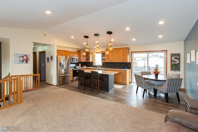 kitchen featuring lofted ceiling, a kitchen island, decorative light fixtures, stainless steel appliances, and a kitchen bar