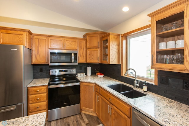 kitchen with vaulted ceiling, light stone counters, backsplash, stainless steel appliances, and sink