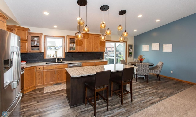 kitchen with sink, a kitchen island, decorative light fixtures, appliances with stainless steel finishes, and dark hardwood / wood-style flooring