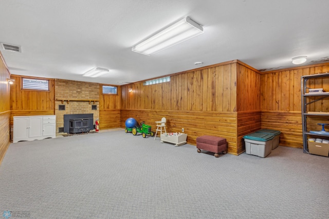 living area featuring a wood stove, carpet, wooden walls, and a fireplace