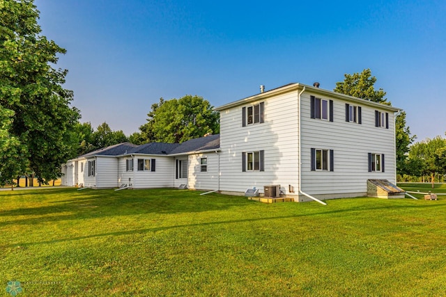 back of property with central AC unit and a yard