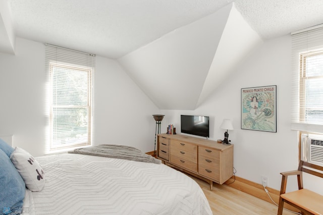 bedroom featuring a textured ceiling, light hardwood / wood-style flooring, and vaulted ceiling