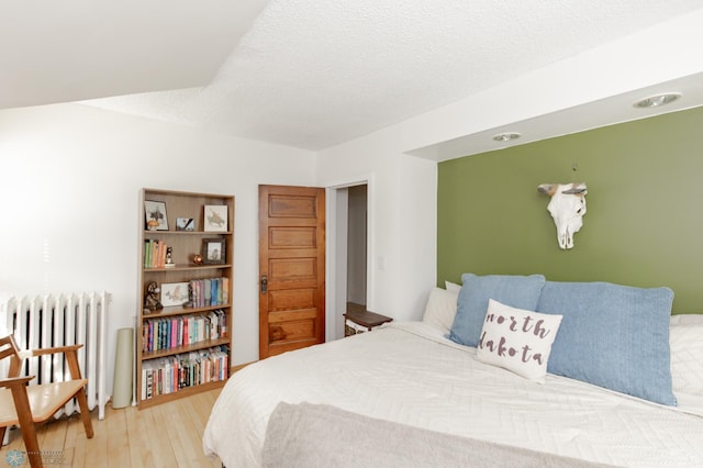 bedroom with wood-type flooring, radiator, and a textured ceiling