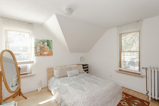 bedroom featuring light wood-type flooring, multiple windows, radiator, and vaulted ceiling