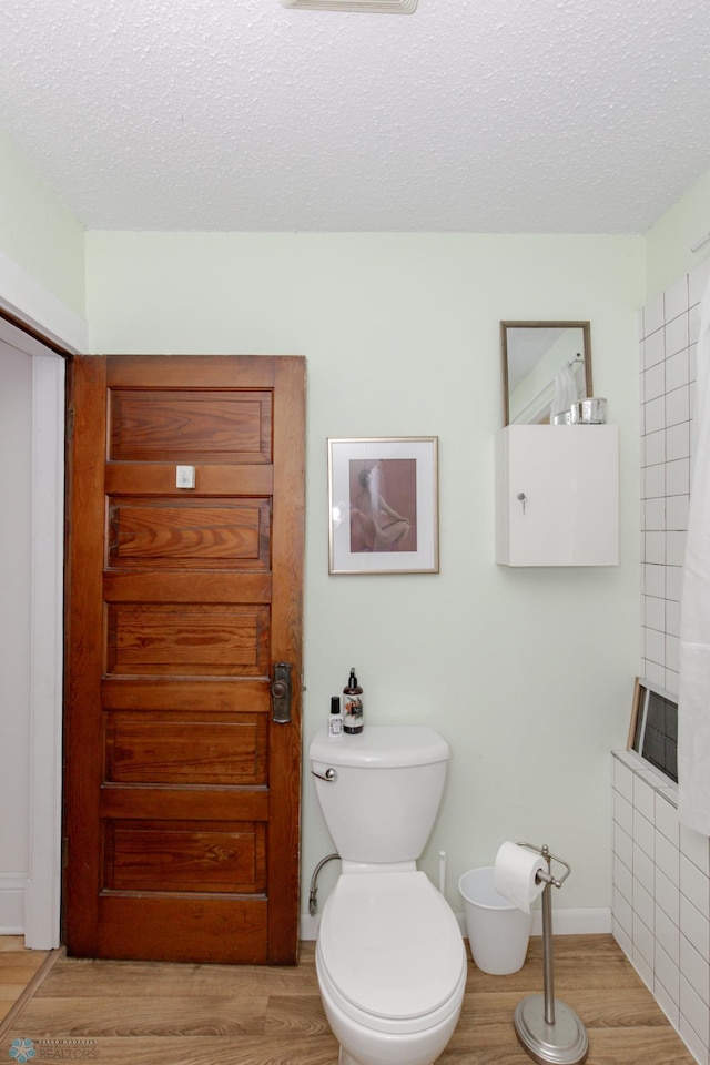 bathroom with a textured ceiling, toilet, and wood-type flooring