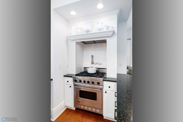 kitchen with light hardwood / wood-style floors, tasteful backsplash, white cabinets, dark stone counters, and luxury range