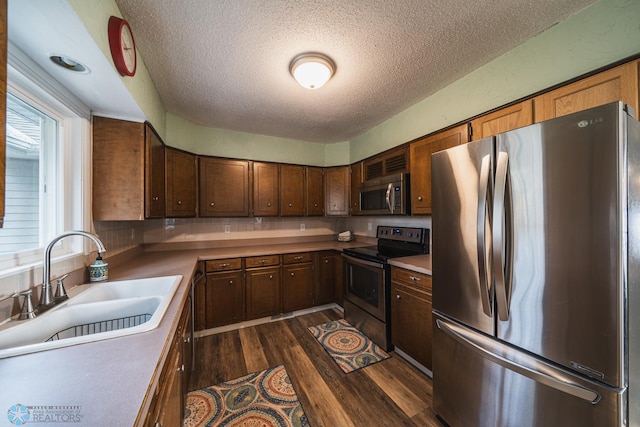 kitchen with sink, a textured ceiling, stainless steel appliances, and dark hardwood / wood-style floors