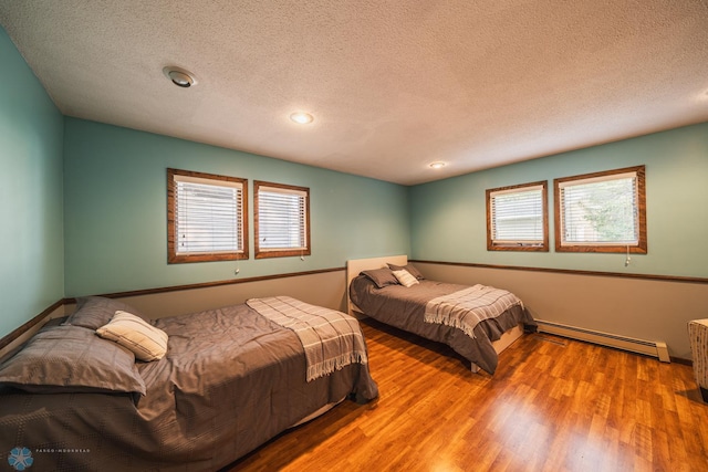 bedroom featuring multiple windows, a textured ceiling, a baseboard radiator, and hardwood / wood-style floors