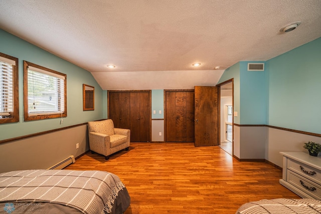 unfurnished bedroom featuring lofted ceiling, light hardwood / wood-style flooring, a textured ceiling, and a baseboard radiator