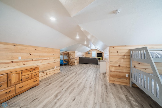 bedroom featuring light wood-type flooring, a textured ceiling, lofted ceiling, and wooden walls