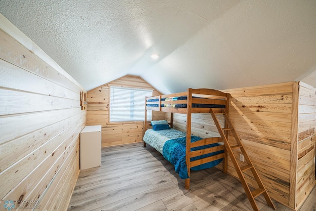 bedroom with lofted ceiling, light hardwood / wood-style flooring, a textured ceiling, and wood walls