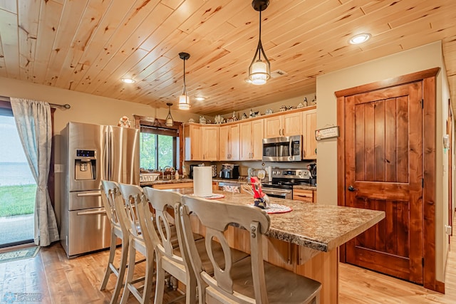 kitchen featuring light brown cabinets, light hardwood / wood-style floors, hanging light fixtures, stainless steel appliances, and a kitchen bar